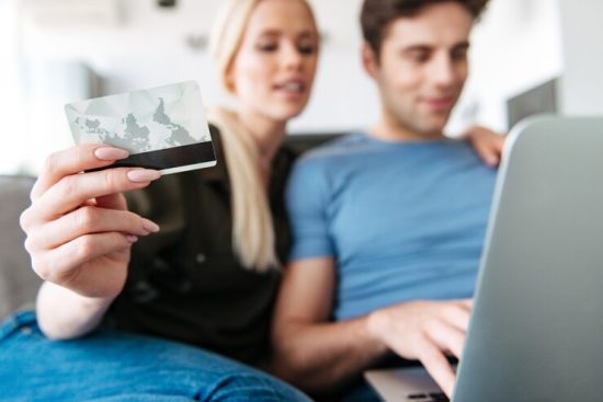 close-up-young-woman-holding-credit-card-while-using-laptop-with-her-husband_171337-4114