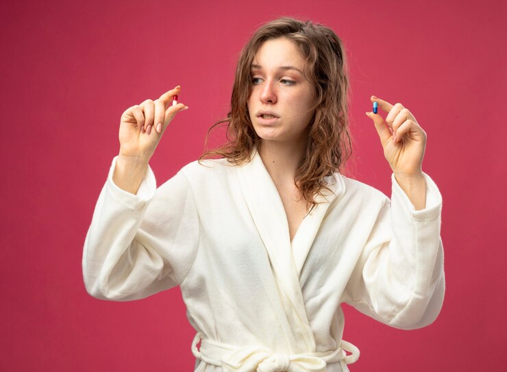 pensive-young-ill-girl-wearing-white-robe-holding-looking-pills-isolated-pink_141793-86350