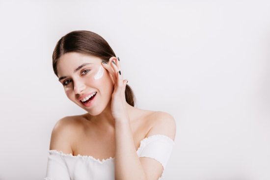 smiling-green-eyed-girl-puts-cream-clean-face-brunette-white-top-posing-isolated-wall_197531-13902