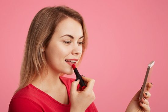 female-lady-paints-lips-with-red-lipstick-uses-smart-phone-as-mirror-prepares-date-with-handsome-man_176532-9650