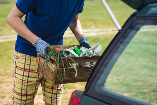 close-up-gardener-holding-vegetable-crate-near-car_23-2147844351